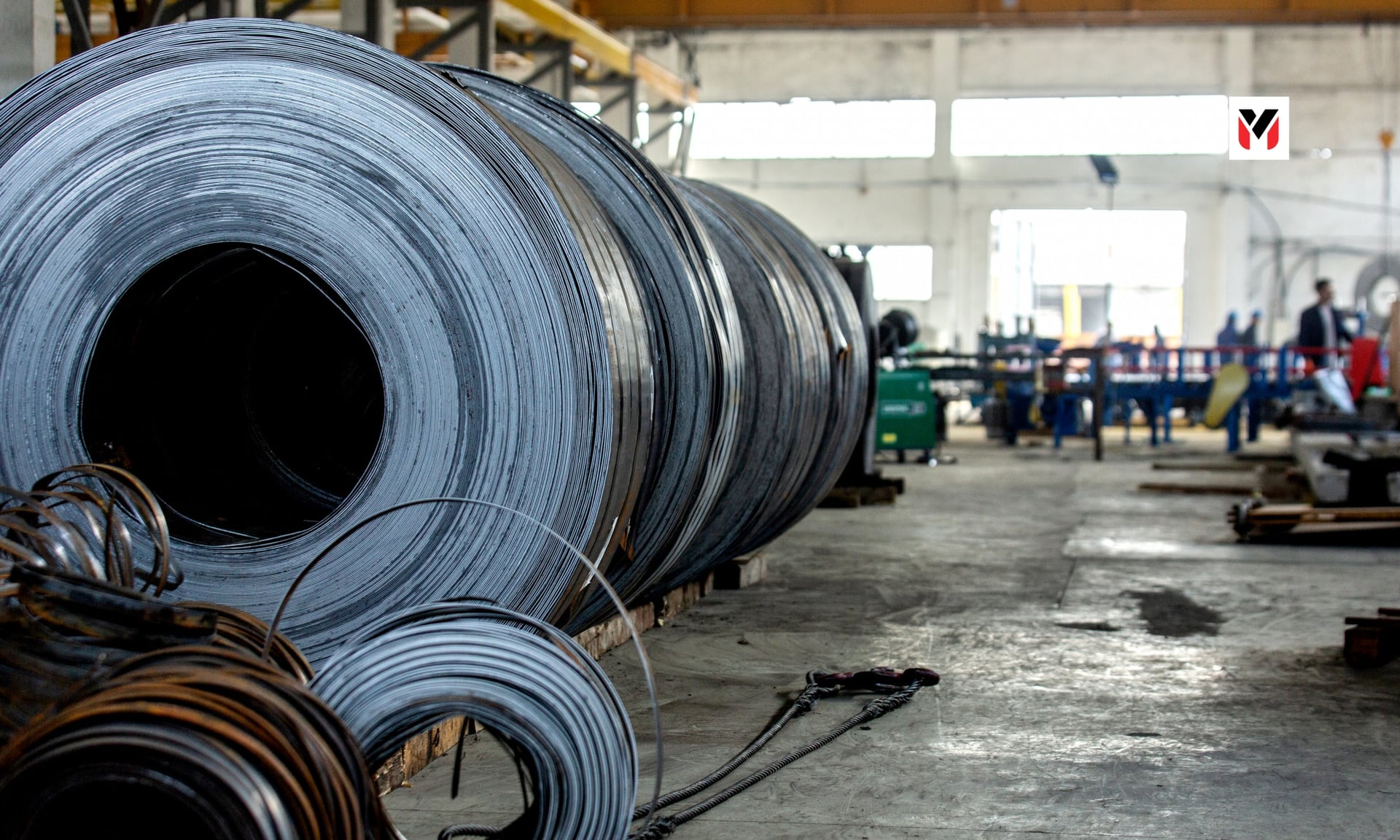 Editorial illustration: a steel coil with arrows pointing out of India larger than arrows pointing in, charcoal and red palette, 16:9.
